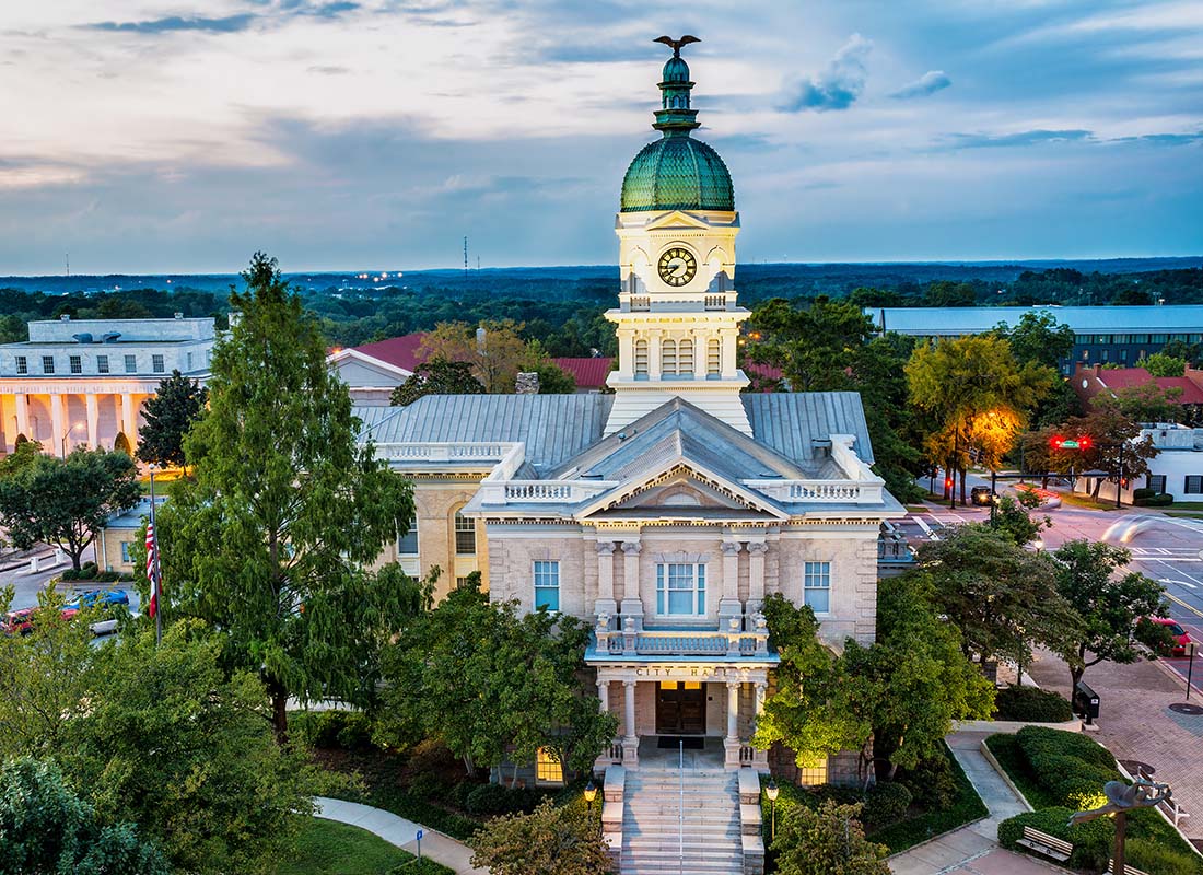 About Our Agency - View of the City Hall Building in Downtown Athens Georgia Surrounded by Bright Green Foliage in the Evening with a Cloudy Sky