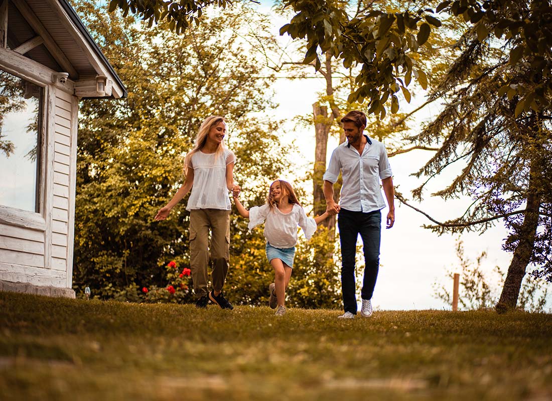 Personal Insurance - Portrait of Smiling Young Parents Holding Their Daughters Hand as They Walk on the Green Grass Outside Their Home on a Sunny Day